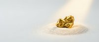 Gold nugget resting on white sand with natural sunlight, symbolizing wealth, treasure, and precious metal mining for financial and business concepts.