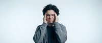 Young Asian man experiencing severe headache holding head with both hands showing pain and stress on white background.