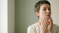 Young Caucasian woman with short pixie haircut touching neck and throat area, checking for swollen lymph nodes or thyroid issues in medical examination.