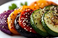 Colorful grilled vegetable slices arranged in rainbow pattern with sesame seeds and herbs on white plate, macro shot showing texture and freshness.