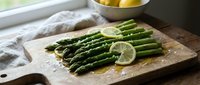 Fresh green asparagus spears with lemon slices on wooden cutting board, healthy vegetable side dish ready for cooking or serving in bright kitchen setting.