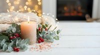 Cozy winter holiday scene with burning candle, eucalyptus leaves, red berries and warm bokeh lights creating festive Christmas atmosphere at home.