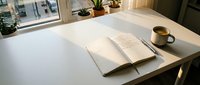 Minimalist workspace with open notebook, pen, and coffee cup on white desk by window with natural light and plants.
