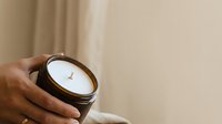 Open jar with white cream or cosmetic product held in male hand against neutral beige background, suitable for skincare, beauty, and wellness marketing.