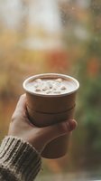 Hand holding hot chocolate with marshmallows in autumn setting, cozy seasonal drink for cold weather comfort and warmth.