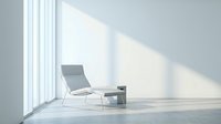 Modern minimalist lounge chair in bright sunlit room with white walls and large windows creating geometric shadow patterns on floor for interior design.