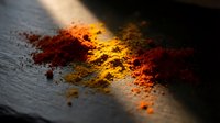 Colorful spice powder scattered on dark slate surface with dramatic lighting creating warm golden glow for culinary cooking and food preparation concepts.
