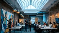 Modern creative office space with diverse team collaborating in industrial loft featuring exposed brick walls, glass ceiling and contemporary artwork.