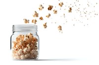 Fresh popcorn kernels exploding out of glass mason jar on white background, creating dynamic motion effect of scattered snack pieces. Isolated food photography.