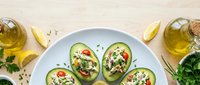 Halved avocados topped with quinoa, cherry tomatoes, feta cheese, and fresh herbs, served with lemon wedges and olive oil on a light wooden surface for healthy eating and nutrition content.