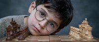 Young boy with glasses lying next to chess board with wooden pieces, contemplating strategic move in intellectual game for educational content.