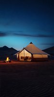 Illuminated luxury glamping tent in desert landscape at dusk with campfire and starry sky, mountains silhouetted against blue twilight atmosphere.