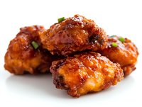 Crispy spicy chicken wings glazed with sweet and tangy sauce, garnished with fresh herbs on white background, close-up view for food photography and menu design.