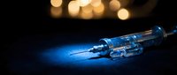 Medical syringe with needle on dark surface with warm bokeh lights in background for healthcare and vaccination concepts.