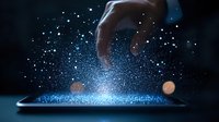 Magical glowing particles rising from digital tablet screen as hand reaches towards sparkling blue light effect against dark background. Digital transformation concept.