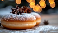 Fresh donut dusted with powdered sugar and decorated with star anise on rustic wooden surface against blurred bokeh lights background, cozy winter mood.