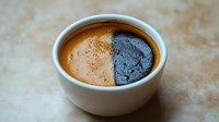 Artistic coffee crema split in half showing light and dark contrast in white ceramic cup on textured beige surface, macro photography of espresso detail.