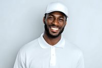 Happy African American man in white polo shirt and cap smiling at camera against gray background for professional headshot and marketing materials.