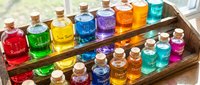 Collection of colorful liquid potions and elixirs in glass bottles with cork stoppers arranged on wooden tray, featuring vibrant rainbow hues for magical, fantasy, or apothecary themed designs.
