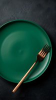 Empty green plate with bronze fork on dark textured surface, ideal for restaurant menus, food styling, dining concepts, and culinary design projects.