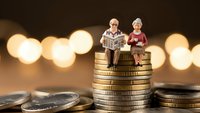 Senior couple figurines sitting on stack of golden coins with warm bokeh lights background representing retirement savings and financial planning.