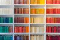 Colorful books arranged by spectrum colors on white library shelves creating rainbow pattern, organized collection of hardcover volumes for education and reading.