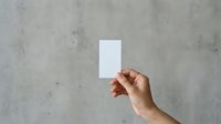 Hand holding blank white card against textured concrete wall background. Suitable for business cards, invitations, promotional materials, and marketing mockups.