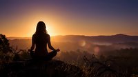 Woman silhouette meditating in lotus pose during golden sunrise over mountain landscape. Peaceful yoga practice for mindfulness and spiritual wellness.