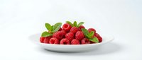 Fresh red raspberries with green leaves arranged on white plate against neutral background, isolated for food and culinary design projects.