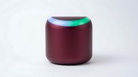 Burgundy smart speaker with glowing multicolor LED ring on white background, isolated wireless audio device for home automation and music streaming.