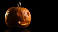 Carved Halloween pumpkin jack-o-lantern with glowing candle light inside on black background for autumn holiday decoration and spooky seasonal celebrations.