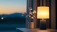 Cozy evening atmosphere with table lamp and cotton plant in vase against sunset window view. Minimalist home decor creates peaceful ambiance.