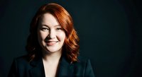 Professional redhead businesswoman smiling confidently in dark suit against black background for corporate headshots and business presentations.