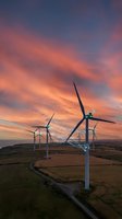 Wind turbines generating renewable energy at sunset with dramatic orange and purple sky over rural landscape for sustainable power concepts.