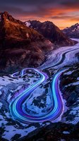 Aerial view of winding mountain road with neon light trails at sunset, snow-covered alpine landscape with dramatic orange and purple sky, long exposure highway photography.