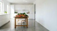 Modern minimalist kitchen interior with wooden island table displaying fresh vegetables and fruits for healthy cooking and meal preparation.