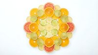Colorful citrus fruit slices arranged in circular mandala pattern on white background. Orange, lemon, lime and grapefruit creating vibrant geometric design.