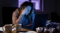 Exhausted young Asian woman working late at night on laptop, holding head in hands showing burnout and stress from overtime work deadlines.