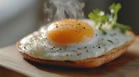 Steaming sunny side up egg on toasted bread garnished with fresh microgreens and black pepper, close up view on wooden cutting board. Morning breakfast.