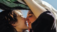 Young diverse couple sharing intimate kiss outdoors in natural sunlight, romantic relationship moment with warm golden hour lighting and soft focus background.