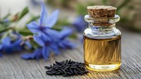 Small glass bottle with essential oil and blue flowers on wooden background with scattered black sunflower seeds, natural aromatherapy and wellness concept.