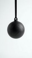 Black spherical pendant lamp with geometric pattern hanging on cord against white background for modern interior lighting design.