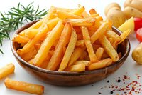 Crispy golden french fries served in rustic wooden bowl with fresh rosemary, raw potatoes and red chili flakes, photographed on white background for food menu.