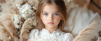 Young girl with blue eyes wearing white lace dress, surrounded by soft beige pampas grass and dried flowers in dreamy natural light setting.