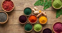 Colorful superfood powders and seeds in wooden bowls on rustic table with moringa leaves for healthy nutrition and wellness supplements.