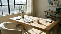 Wooden desk with natural light from large windows, featuring minimalist workspace with potted plants, notebooks, and office supplies in bright, airy home office setting.
