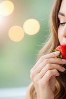 Young blonde woman enjoying fresh strawberry with soft bokeh lights background creating dreamy atmosphere for healthy eating and wellness concepts.