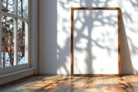 Empty wooden frame on rustic floor near window with natural tree shadow overlay creating artistic composition, sunlight streaming through glass panes.