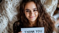 Young Hispanic woman with long curly dark hair and bright smile holding thank you note card against white lace background, expressing genuine gratitude and appreciation.