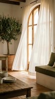Bright sunlit interior with arched wooden door, flowing white sheer curtains, potted olive tree, olive green upholstered seating, and rustic wooden furniture creating a serene Mediterranean-inspired living space.